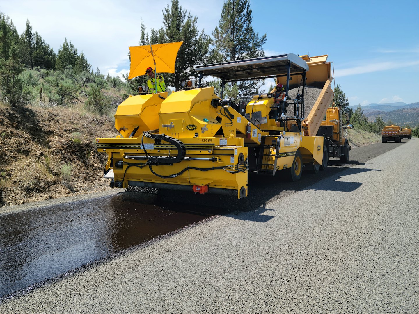 Bauarbeiter legen mit Asphaltiermaschinen Asphalt auf eine Straße.